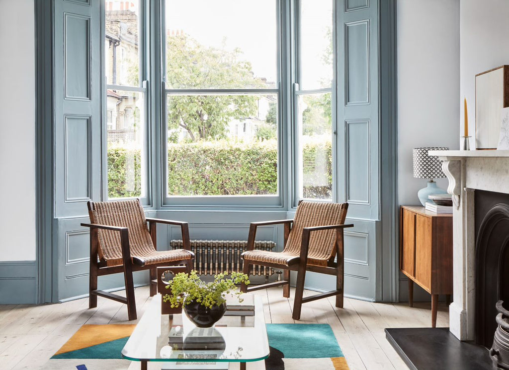 a living room with open windows, chairs, and small table